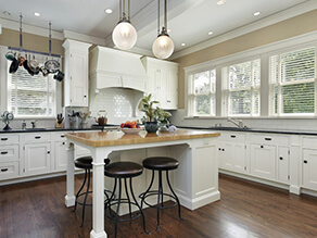 Classic_Polished_Kitchen_White_Island_tan_wall_white_cabinets_black_stools_plant_pots_pans